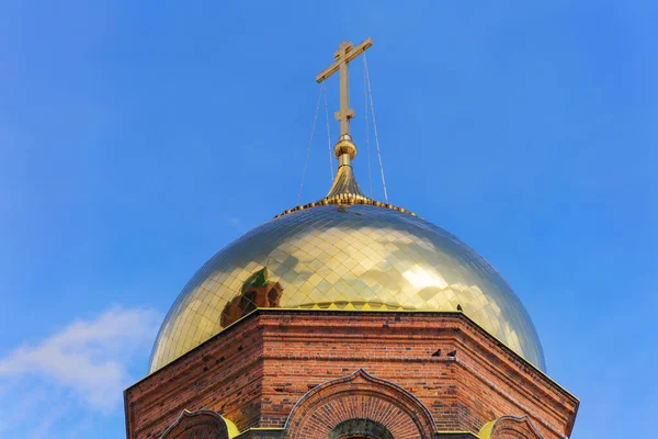 The golden dome of the old brick church. Close-up, bottom view. Sunny day and blue sky. The sun reflects on the golden surface of the dome. Ancient rural church in traditional style. Ural (Russia)