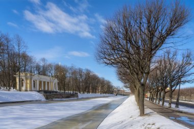 Bahar şehri manzarası, yarı donmuş bir nehir, çağlık dallanan ağaçlarla dolu sokaklar, sütunları ve mavi ve beyaz gökyüzü olan eski bir taş pavyon. St. Petersburg 'da (Rusya) güneşli bir gün. Baharın başlarında 