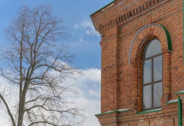 Güneşli bir bahar gününde, Rusya 'nın Mezenskoye köyündeki (Orta Ural, Rusya) antik bir kilisenin pencerelerinden birinde. Yakın plan. Tarihi kilisenin ön cephesinin ayrıntıları. Kabartmalı tuğla duvarlar, kemerli pencereler