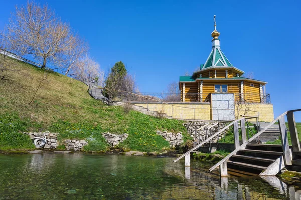 A chapel at a source of clean spring water in the village of Bolshie Klyuchi (Perm Territory, Russia) on a sunny spring day. A bathing lake formed by several springs with the purest water. Early May, fresh herbs