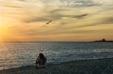Deniz kıyısında gün batımı. Sarı-turuncu gökyüzü, giden güneşin ışınlarıyla aydınlatılır. Bir kız kıyıda oturur (arkadan bakar) ve renkli günbatımına hayran kalır. Bir martı gökyüzünde süzülür 
