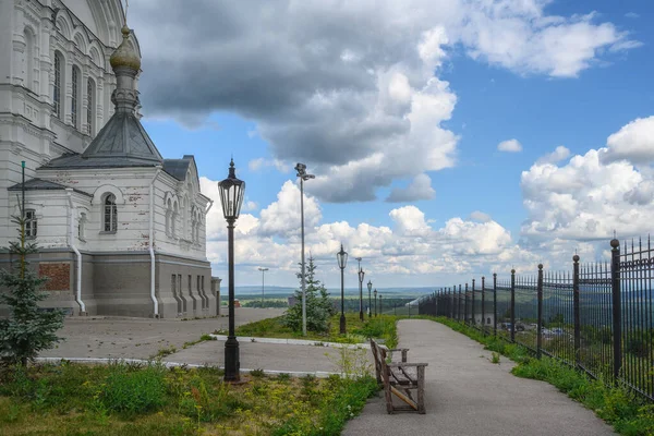 夏の日にBelogorsk Monastery ロシアのPerm Territory にランタンとベンチがある路地の1つ 古代の教会とキャストフェンスの壁が表示されます 雲のある青空 — ストック写真