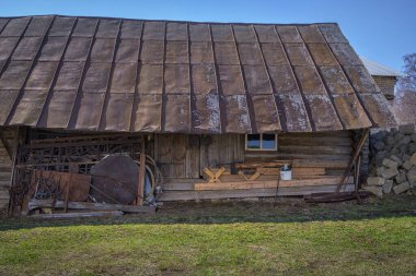 Güneşli bir bahar gününde zaman ve yağmurla kararmış bir kır kütüğü. Antika desenli metal çatı, işlenmiş demir elementli kapılar. Ahırın yakınındaki çiftlikte gerekli şeyler. Mavi gökyüzü. Rusya, Ural 