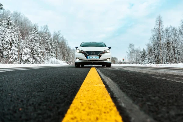Aluksne, Letonya - 01.12.2021 metalik beyaz Nissan Yaprağı asfalt yolda, kışın sarı çizgilerle. Nissan tarafından üretilen beş kapılı hatchback elektrikli araba.