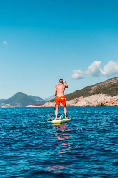 A young athletic man stands on a SUP stand up paddle board in blue water sea in Montenegro