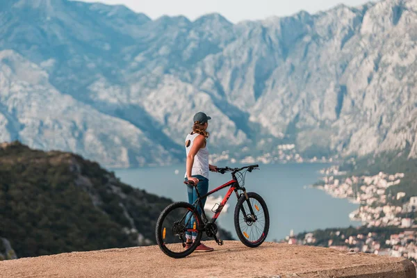 Young athletic woman cycling on a cliff overlooking Kotor bay (Boka Kotorska), Montenegro, Europe