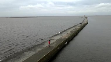 Young Asian man rides a onewheel, electric skateboards along a jetty along the sea. 4K Aerial drone view