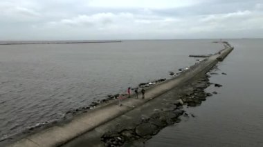 Young people ride onewheel, electric skateboards along the jetty along the sea. 4K Aerial drone view