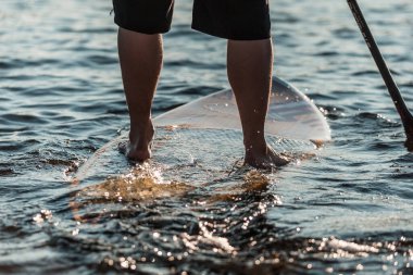 Suya batırılmış bir SUP 'nin üzerinde duran bir adama yaklaş.