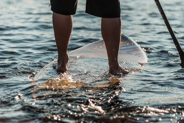 Suya batırılmış bir SUP 'nin üzerinde duran bir adama yaklaş.