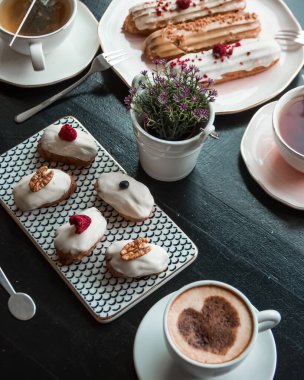 Geleneksel Fransız tatlıları. Kafe veya restoranda siyah masada beyaz çikolatalı ekler. Sıcak çikolata içeceği ve yakında çay.