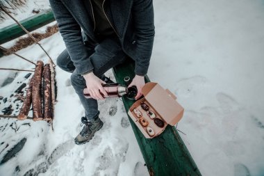Bir adam yeşil bir bankta termostan bir fincan kahve koyuyor ve yanında da geleneksel Fransız tatlı ekini var. Kışın piknik konsepti