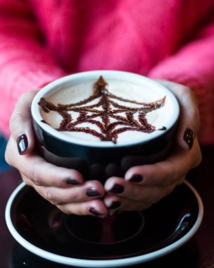 Siyah manikürlü bir kadın elinde örümcek ağları desenli bir kahve kapuçinosu tutuyor, Cadılar Bayramı modunda.