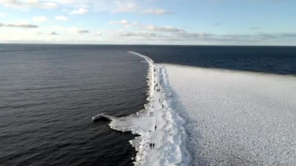 People walk along the icy pier to the orange lighthouse, view from the drone — Wideo stockowe