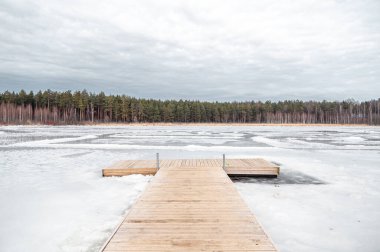 Baharda, buzlar çözülürken donmuş bir gölün üzerinde tahta bir köprü. Balozi belediyesinde Titurgas Gölü