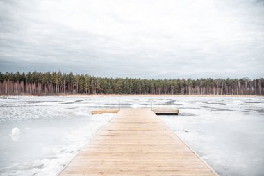 Baharda, buzlar çözülürken donmuş bir gölün üzerinde tahta bir köprü. Balozi belediyesinde Titurgas Gölü