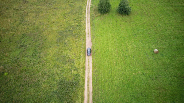 Aerial view of car driving on road around grass fields in countryside