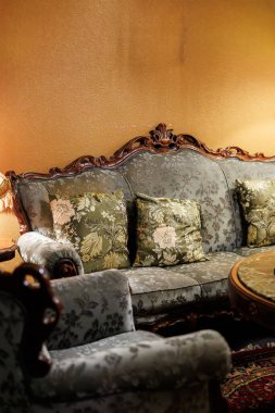 Oyma ahşap kanepe ve döşeme desenli koltuk yuvarlak ahşap budanmış bir masanın yanına otur. Duvarlardaki lamba ışığı rokoko aksanını ve İran tarzı bir halıyı ortaya çıkarıyor..