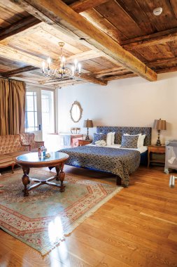 Ilık, aydınlık bir yatak odası çifti geri kazanılmış kereste kirişleri, bir avize, desenli yatak, antika ayna, kıvrık kanepe ve yatak başlığını çerçeveleyen lambalar ile Fransız kapıları..