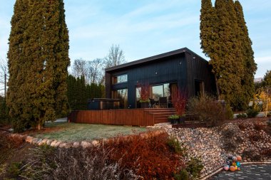 Kutulu bir kömür evi yükseltilmiş bir ahşap güvertede, çimde don, sonbahar çalıları, büyük pencereler, ve samimi bir veranda ile, yemyeşil ve gabion bir duvar üzerinde oturur..