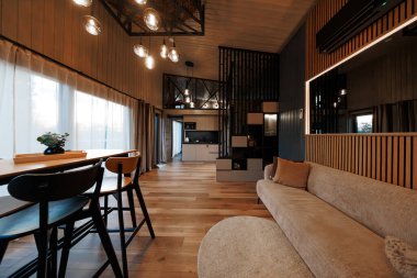 Gün batımında açık bir çatı katı, kubbeli ahşap tavan, baloncuklu kolyeler, küp raflı siyah bölmeli bölme, bej kanepe, yemek tezgahı, ve mat mutfak..