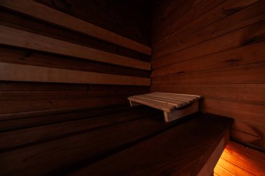 Katmanlı kereste bankları ve gevşek bir başlık, düşük ışık oturumu sırasında tahıl ve düğümleri ortaya çıkaran hafif turuncu bir bankın altında, sedir örtülü bir saunada oturur..