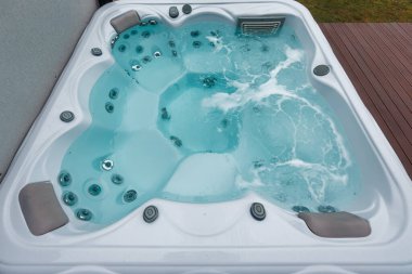 Beyaz dikdörtgen kaplıcalarda dönen turkuaz su, paslanmaz jetler, gri başlıklı lobi koltukları, kontrol düğmeleri ve kaymak girişi var.