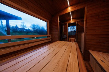 Ahşap panelli kabin içi uzun banklar ve eğimli bir masa, doğrusal LED şeritler kapı aralığı, geniş açı görüşü, alacakaranlık ışığı, panoramik pencere kırsal evleri ve çıplak ağaçları gösteriyor.