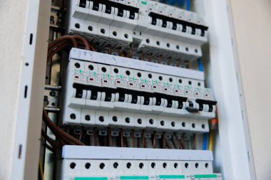 Çoklu sıra minyatür devre kesiciler on şalter, kahverengi ve mavi iletkenler, DIN demiryolu montajı, numaralandırılmış terminaller ve bir kapalı hizmet alanında yan ışıklandırmayı gösterir.