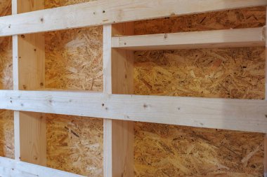 Hafif çam çivileri ve yatay noggins çerçeve OSB panelleri. Taze kesikler, düğümler ve vida delikleri, ışık altında bile iç yapının sıcak olduğunu gösteriyor..