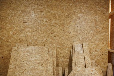 Bir atölyede kesilen iplik levhaları OSB duvarına dayanır. Sıcak yapay ışık ahşap taneciklerini ve reçineyi ortaya çıkarır. Paneller çerçevelenmeyi ya da kabine hazırlanmasını beklerken..