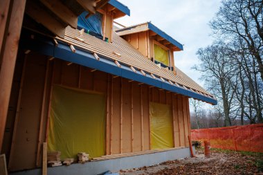 İnşaatçılar, yapraksız ağaçlarla çevrili bir arazide kereste evlerinde çalışıyorlar. Açığa çıkmış çiviler, iki yatakhane, mavi kanat yanıp sönen, sarı mühürlü açıklıklar, ve bulutlu ışık altında çatı yarasaları görünür..