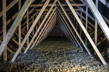 Üçgen tavan arası, tekrar eden ahşap kirişleri ve metal gübre kaplamaları gösteriyor. Gevşek selüloz serin, dağınık ışık altında zemin kaplayan kapalı teftiş sahnesi.