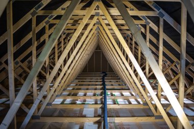 Yeni inşa edilen tavan arasında tekrar eden ahşap kirişler, metal plakalar ve koyu buhar bariyeri var. Tek bir esnek kanal izole zemin panellerinin üzerinde gün ışığında..