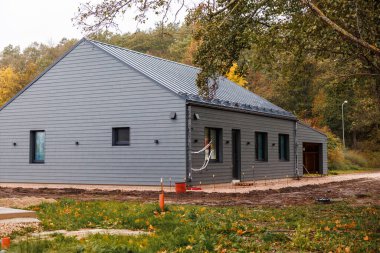 Gri kaplamalı tek katlı çatı katı, metal çatı oluğu, küçük pencereler ve sağ taraftaki garaj. Sonbahar yaprakları ve bulutlu ışıkla yeni derecelendirilmiş arsa.