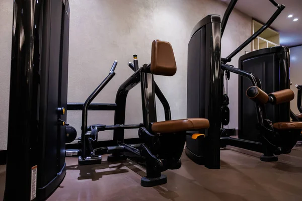Kahverengi pedli bir dizi siyah seçilmiş makine modern bir spor salonunda duruyor. Yastıklı koltuklar ve sarı iğneli ağırlık yığınları yumuşak, hatta ışık altında bile görülebilir..