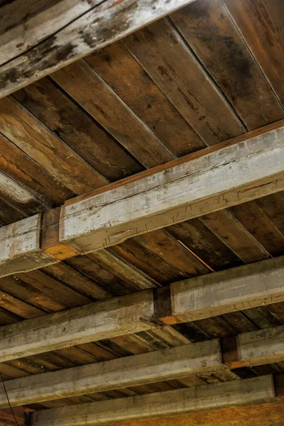 Ağır ahşap kirişleri ve kalasları yakından görmek testere izleri, çivi başları ve su lekelerini gösteriyor. Ilık yönelimli ışık, içinde ışık görünen ve yaşlanan işçilik ile boşlukları ortaya çıkarır.