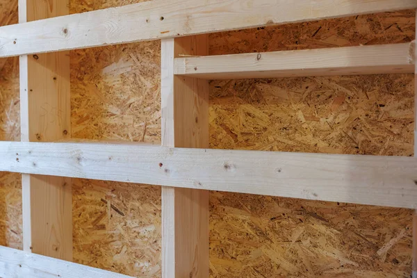 Hafif çam çivileri ve yatay noggins çerçeve OSB panelleri. Taze kesikler, düğümler ve vida delikleri, ışık altında bile iç yapının sıcak olduğunu gösteriyor..