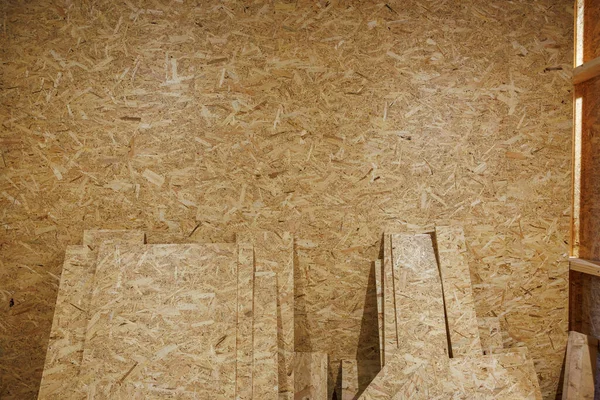 Bir atölyede kesilen iplik levhaları OSB duvarına dayanır. Sıcak yapay ışık ahşap taneciklerini ve reçineyi ortaya çıkarır. Paneller çerçevelenmeyi ya da kabine hazırlanmasını beklerken..