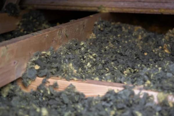 Yakın görüntü tavan arasındaki bitmemiş kirişler arasında selüloz veya mineral yünü gösteriyor. Gri ve sarı lifler yapay ışığın altında sığ bir alan derinliğinde ortaya çıkar..