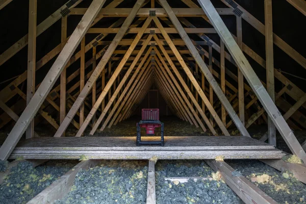 Kırmızı sandalye, tekrar eden ahşap kirişlerin arasında dar bir tavan arası geçidi üzerine kuruludur. Açığa çıkmış kirişler ve metal bağlantı levhaları, alçak akşam ışığı gibi görünen bir tüneli çerçeveler..