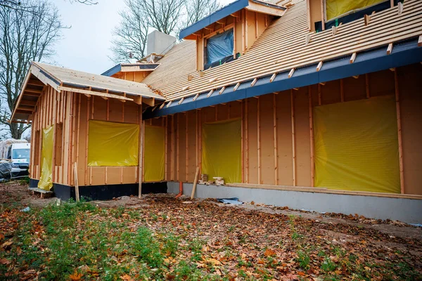 Kısmen inşa edilmiş konutlarda çiviler, kılıflar ve yarasalar görülüyor. Sarı film pencereleri kapatıyor, tepenin yanında baca yükseliyor, minibüs park halinde, sonbahar ağaçları ve yapraklar var..