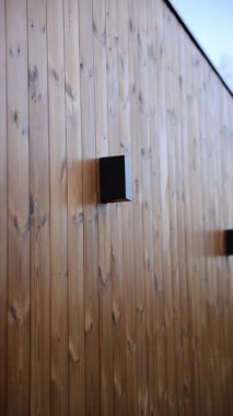 Dikey ahşap kaplama ve iki mat siyah duvar lambası yumuşak dikdörtgen gölgeler oluşturur. Sıcak ballı kahverengi kereste, öğleden sonra güneşi, hafif aşağı doğru hareket.