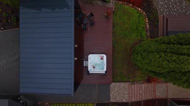 Mavi metal çatısı, güverte jakuzisi ve oyun seti olan bir banliyö evi. Yukarıdan bakıldığında kaldırım sürücüleri, yürüme yolu, kozalak, sonbahar tonları ve düşük ışık havası görülüyor..