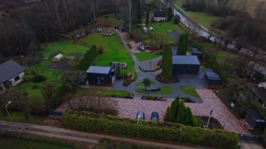 Hava aracı görüntülerinde tuğladan yollar, modüler siyah ek binalar, uzun kozalaklılar, oyun setleri, park edilmiş arabalar, eğimli yürüyüşler, güverteler, sebze bahçeleri, seralar, çalılıklar görülüyor..