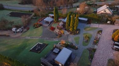 Düşük açılı hava göstergeleri modern ek binalar, desenli tuğla avlular, kıvrımlı yürüyüş yolları, gölet, oyun alanı, beyaz çoklu tüneller ve sabah ışığında Letonya bayrağı gösteriyor..