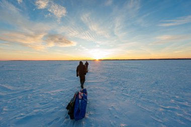 Güneşin doğuşunda donmuş bir gölde iki bohça balığı yürür, çubuklar ve bir çengelle kızak çekerler. Rüzgar şeklinde kar, düz bir ufuk, ve uzak bir ağaçlık çerçeve uzun gölgeler..
