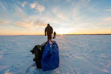 İki bohçalı balıkçı gün doğumunda donmuş bir gölde yürürler, kızakları teçhizat, muşamba ve çengelle çekerler. Yer seviyesi görünümü öncü çizgiler ve sıcak düşük ışık kullanır.