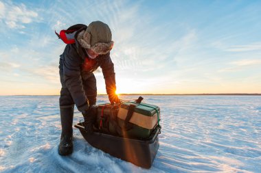 Sarkık bir balıkçı, güneşin doğuşunda donmuş gölü süpüren rüzgarın üzerindeki kızak kayışlarını sıkılaştırır. Güneş kollarında parlar, uzun gölgeler, alçak açı, sıcak arka plan ışığı, kış ortası teçhizatı..