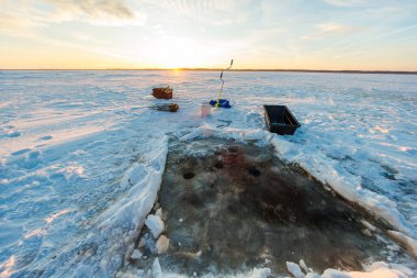 Şafak vakti donmuş bir kuzey gölü delinmiş delikleri, kar bereleri, manuel kumanda, kızak, kova ve uzun gölgeler bırakan alet sandıklarıyla temizlenmiş bir buz deposunu gösteriyor..